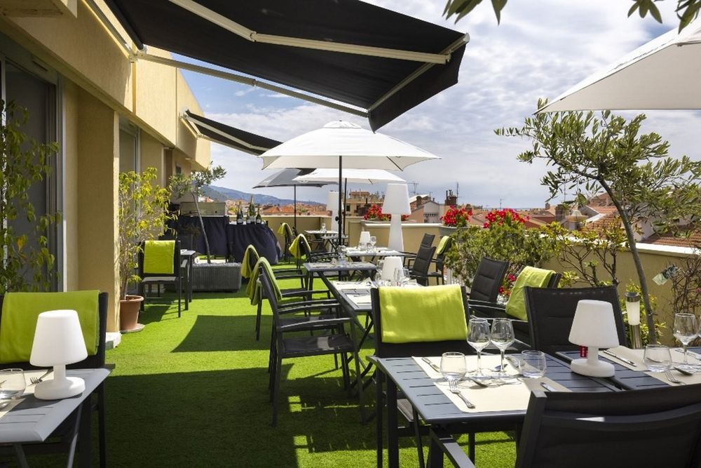 Tables, parasols and green lounge chairs on the rooftop terrace of the Hôtel Méditerranée in Menton