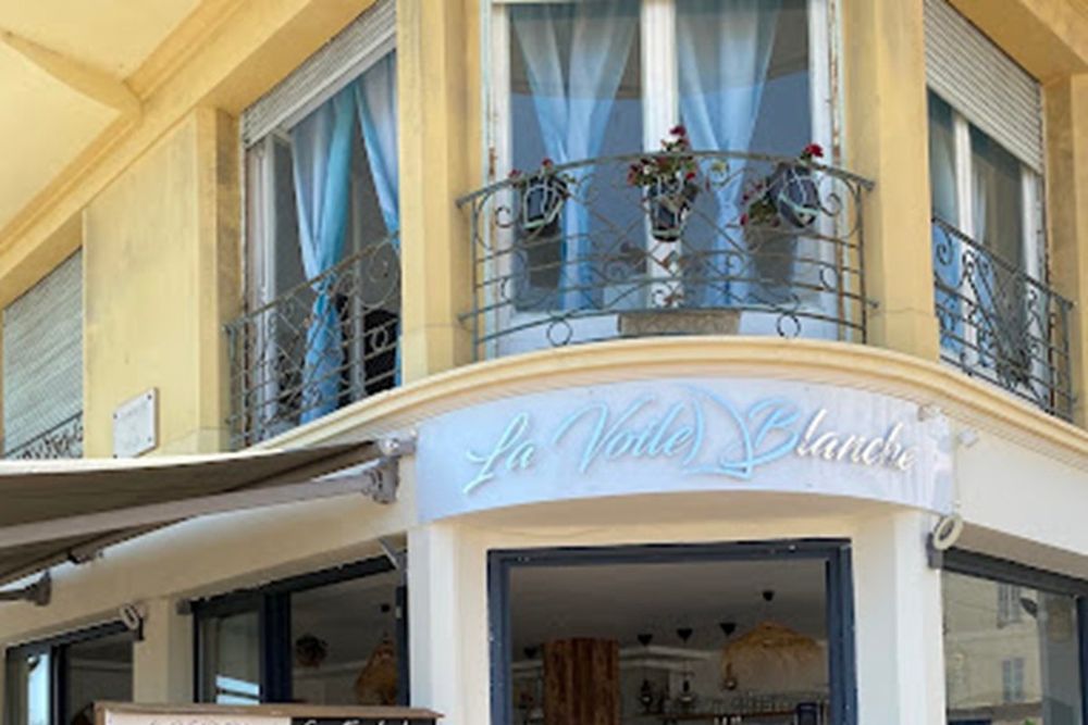 The front of La Voile Blanche restaurant with its sign and wrought-iron balconies in Menton