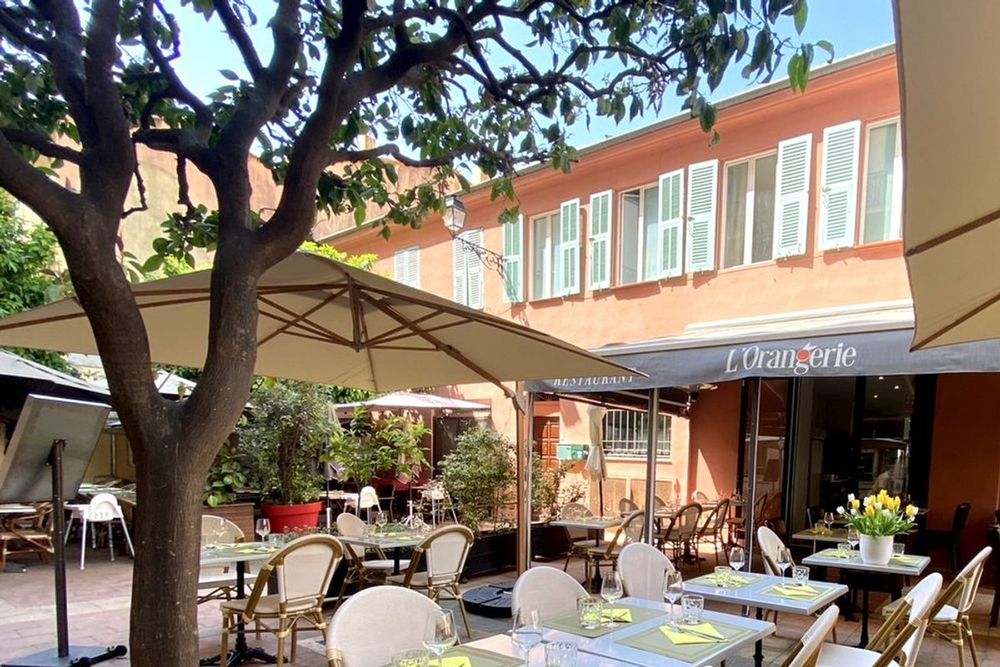 The terrace of L'Orangerie restaurant under a tree on a pedestrian street in central Menton