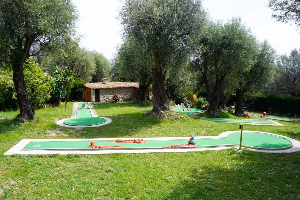 Green mini-golf holes laid out on the lawn under olive trees at the Parc du Pian, Menton