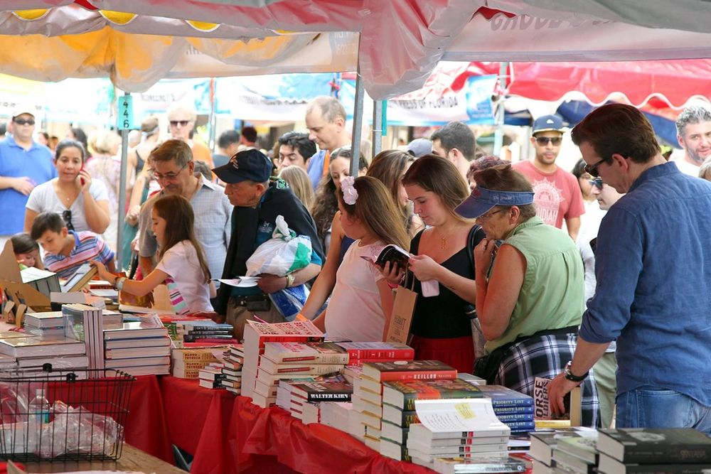 Visitors browsing tables of books under red awnings at the Miami Book Fair street fair