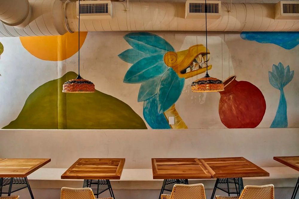 Wooden tables beneath a large painted mural of a bird and fruit in the dining room of Los Félix, Coconut Grove