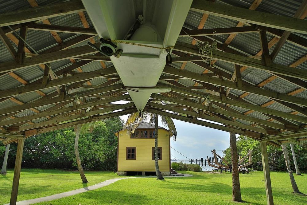 A yellow wooden building seen from under an open-sided shelter on the lawn of The Barnacle, Coconut Grove