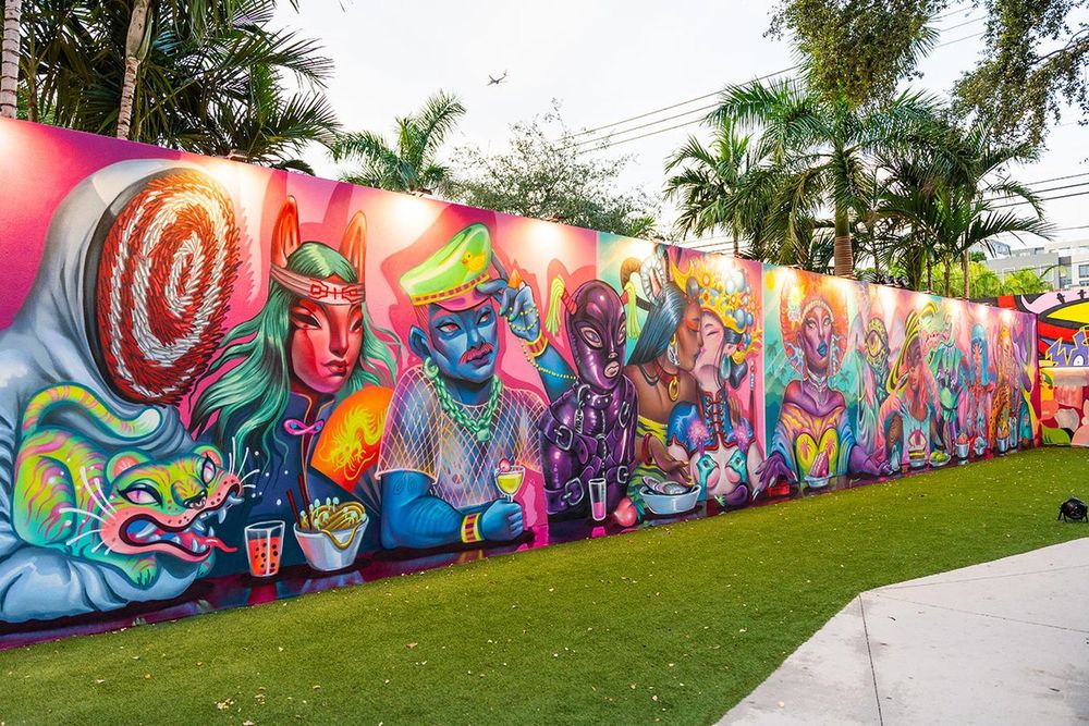 A long, colourful mural of fantastical figures by Lauren YS along a lawn at Wynwood Walls