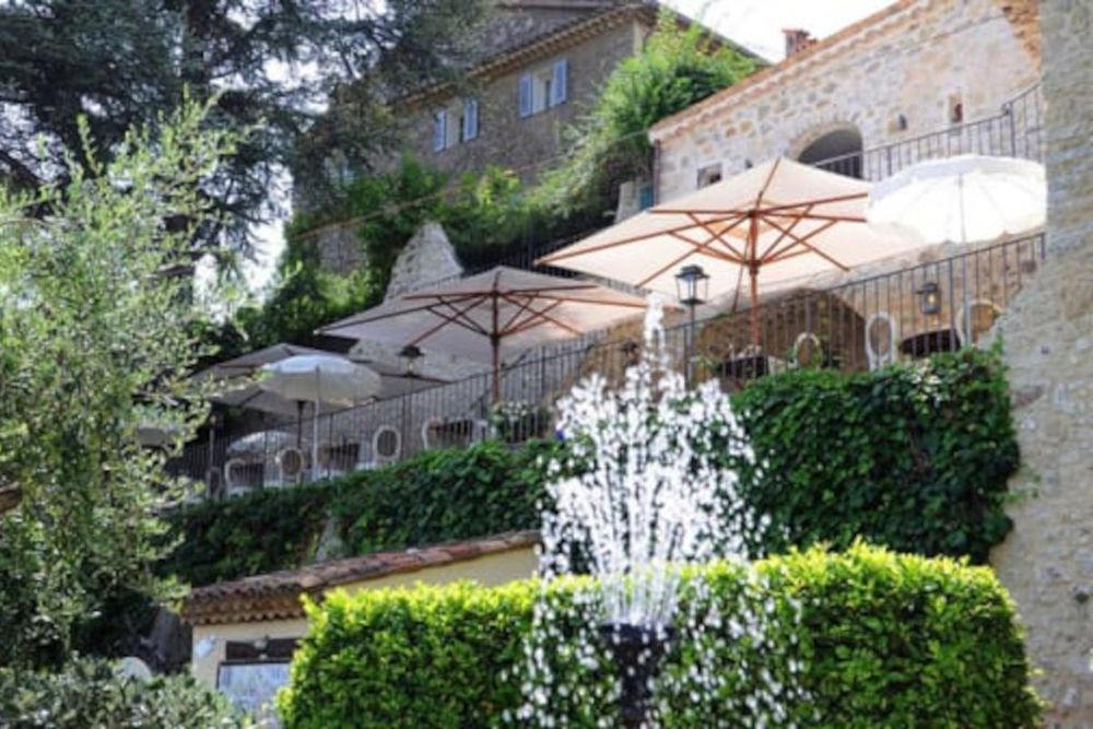 Parasols on the terraced dining area of L'Amandier de Mougins above a garden fountain