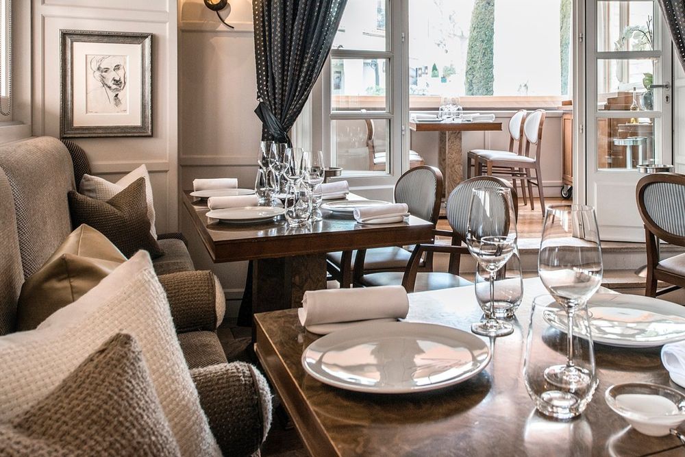 Laid tables and armchairs in the dining room of La Place de Mougins, opening on to the conservatory