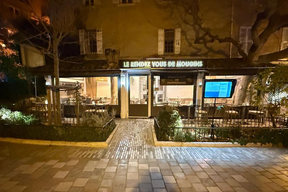 The lit-up terrace and façade of Le Rendez-vous de Mougins on Place du Commandant Lamy at night