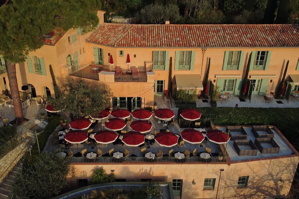 Aerial view of Le Mas Candille's ochre buildings and its terrace of red parasols among the pines