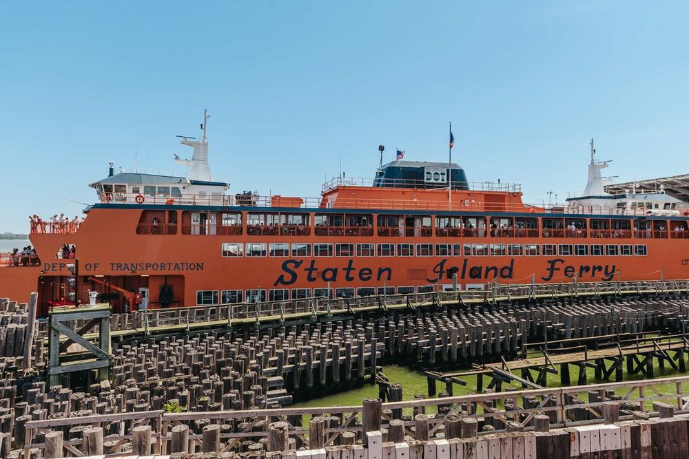 An orange Staten Island Ferry berthed at the terminal under a clear sky
