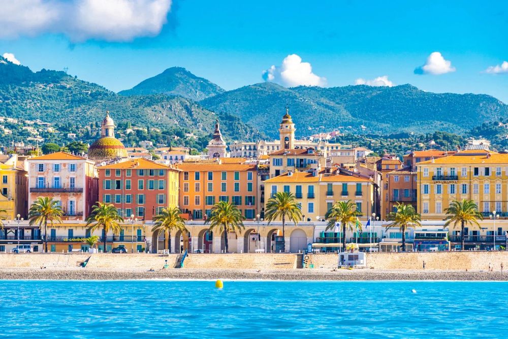 The ochre and pink seafront façades of Vieux Nice above the beach, with the hills behind, seen from the sea