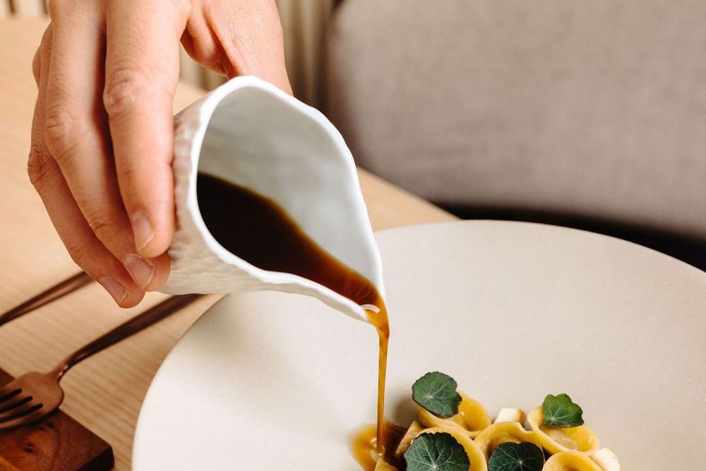 Sauce being poured over a plate of filled pasta with nasturtium leaves at ONICE, Nice
