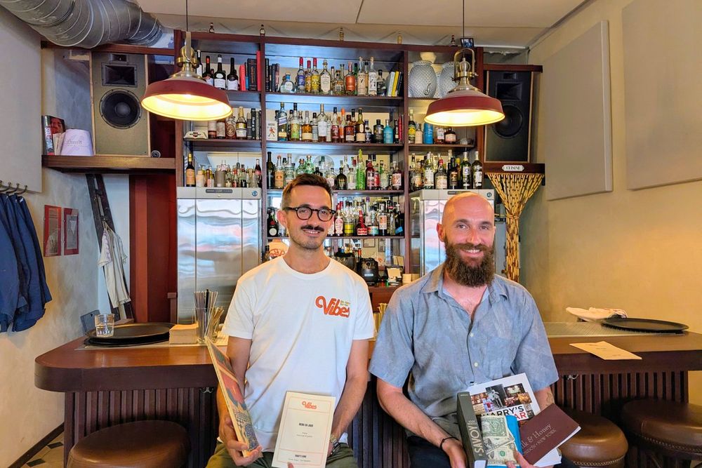Two of the founders of Vibes at their bar near the port of Nice, with the back bar of bottles behind them
