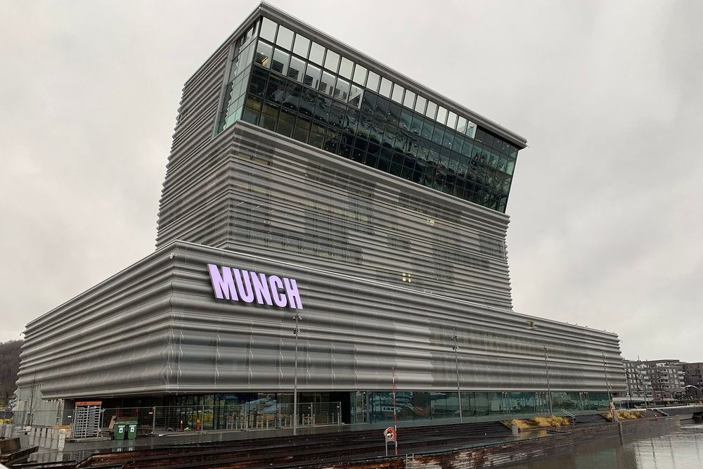 The MUNCH museum tower with its lit name sign seen from the harbourside in Bjørvika