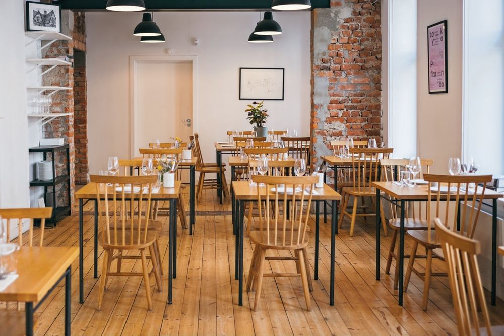 The light, wood-floored dining room of The Little Pickle with brick walls and simple wooden chairs