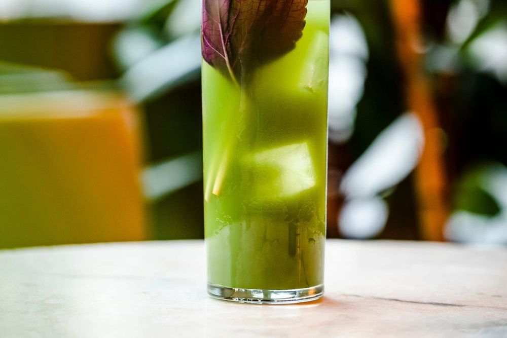 A tall green cocktail garnished with a leaf on a marble table at Torggata Botaniske