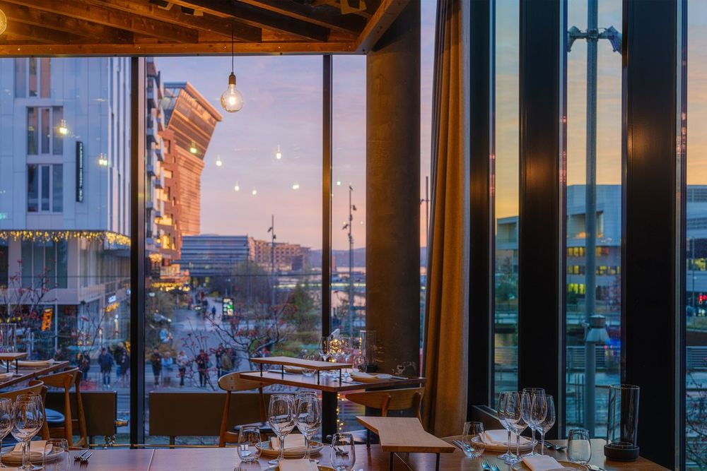 Laid tables by the floor-to-ceiling windows at Vaaghals in Bjørvika, with the evening sky over the Barcode district