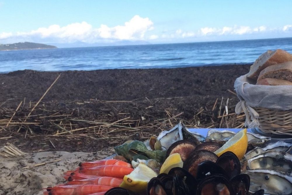 A platter of oysters, prawns and lemons on the sand at Le Migon, with the sea behind
