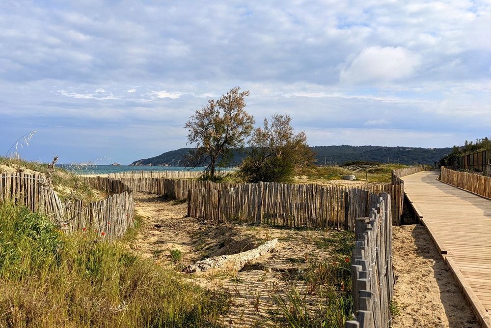 A wooden walkway and fenced sandy path through the dunes towards the sea at Pampelonne