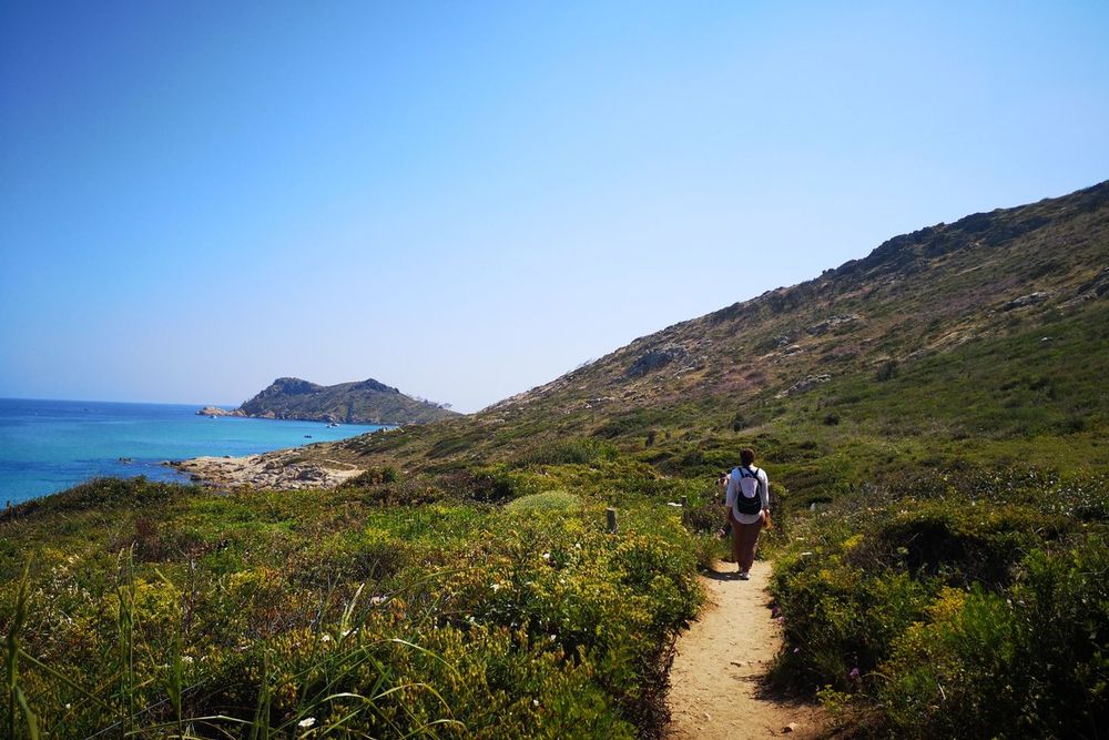 A walker on the path through the maquis towards Cap Taillat, with the sea on the left