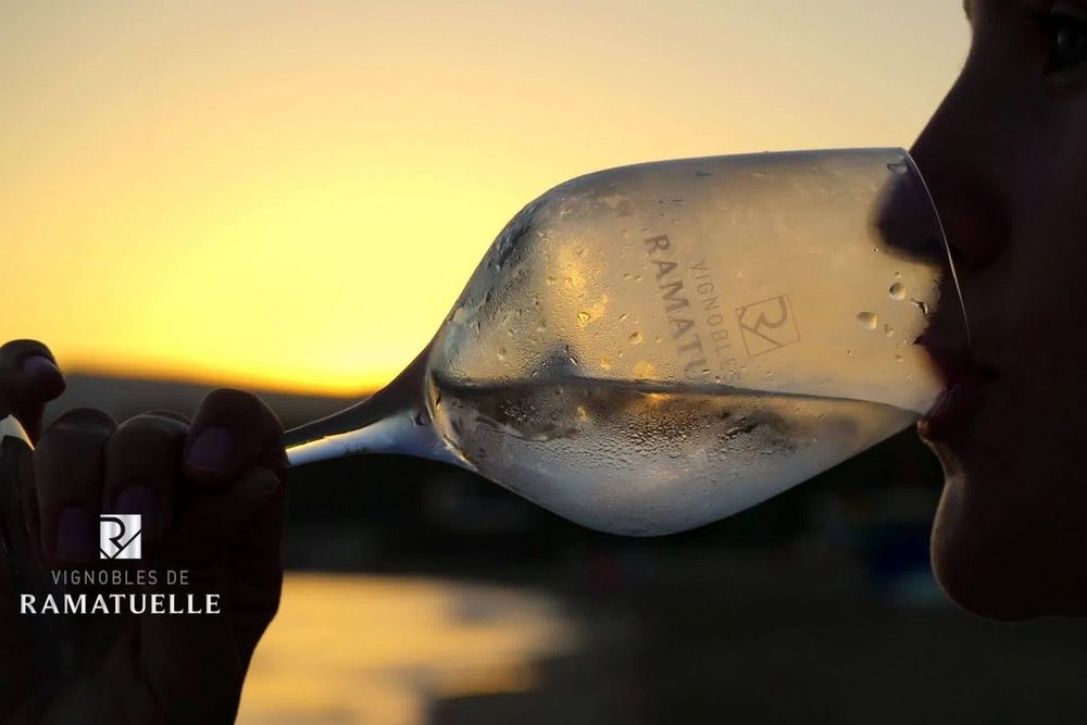 A glass of Vignobles de Ramatuelle wine held up against a sunset sky