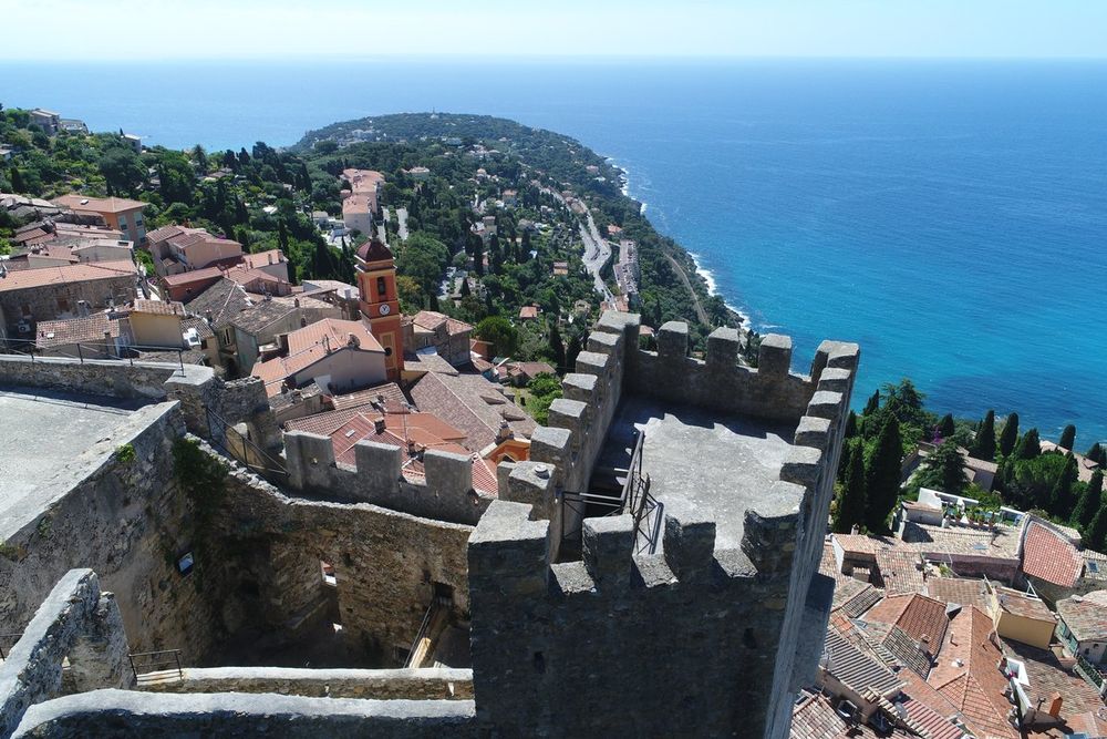 The crenellated keep of Roquebrune castle above the village rooftops, with Cap Martin and the sea beyond