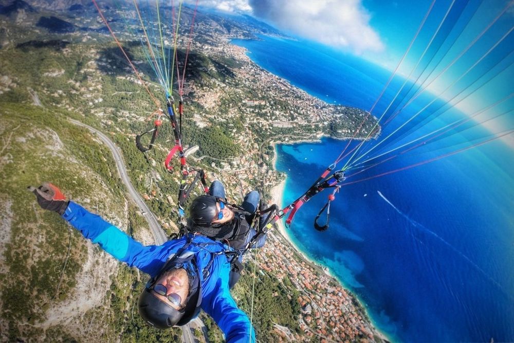 A paraglider pilot in flight above the slopes of Mont-Gros with Cap Martin and the sea below