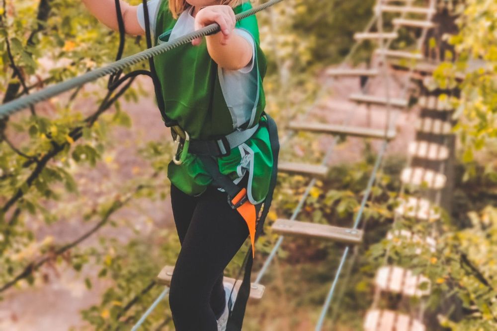A climber in a harness crossing a wooden-step rope bridge among autumn trees at AccroCamp Saint-Germain-en-Laye