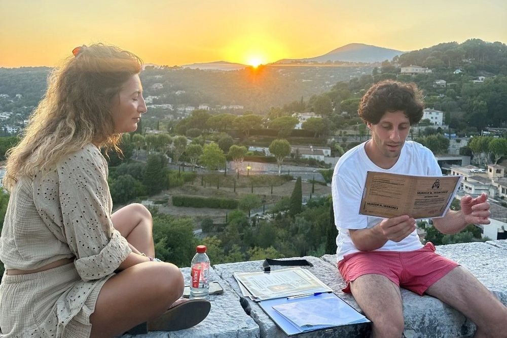 Two players reading case notes on a stone wall at sunset during a live investigation game