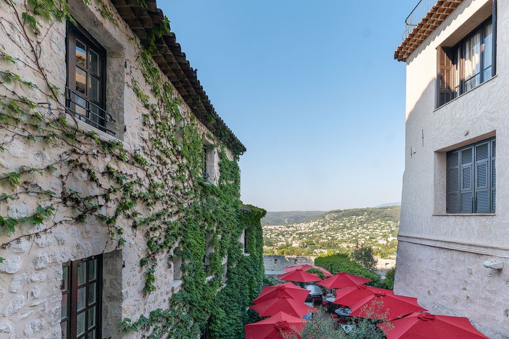 Red parasols on the terrace of the Hôtel Le Saint-Paul between ivy-clad walls, with the hills beyond