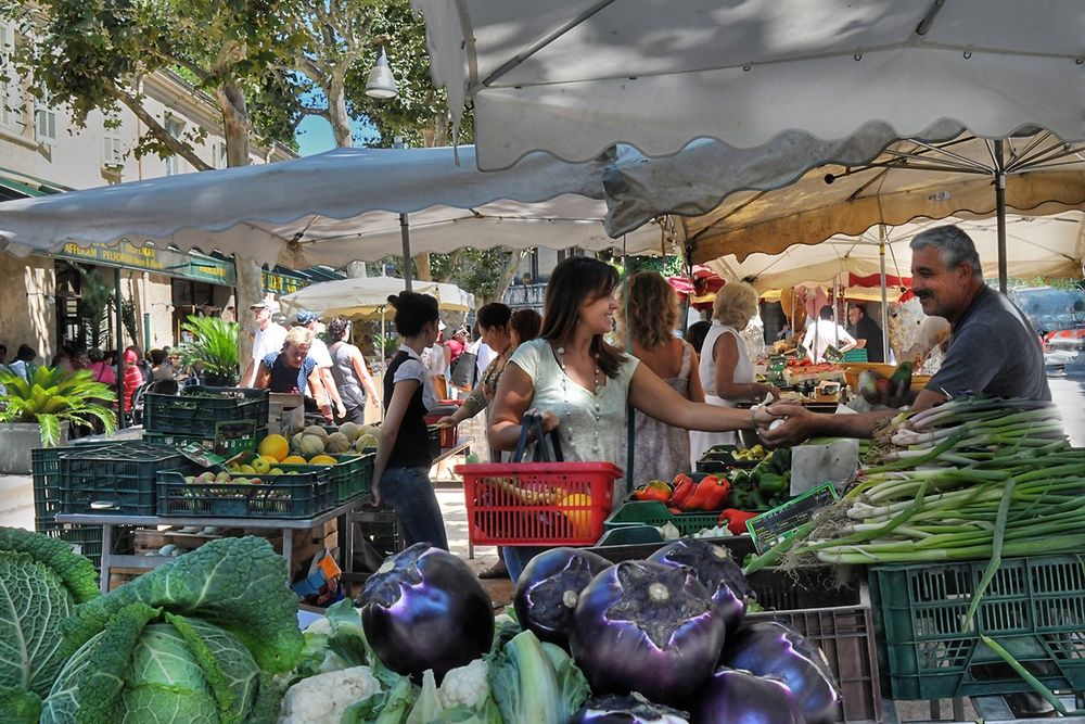 A stallholder serving shoppers over crates of vegetables at the Saint-Paul de Vence market