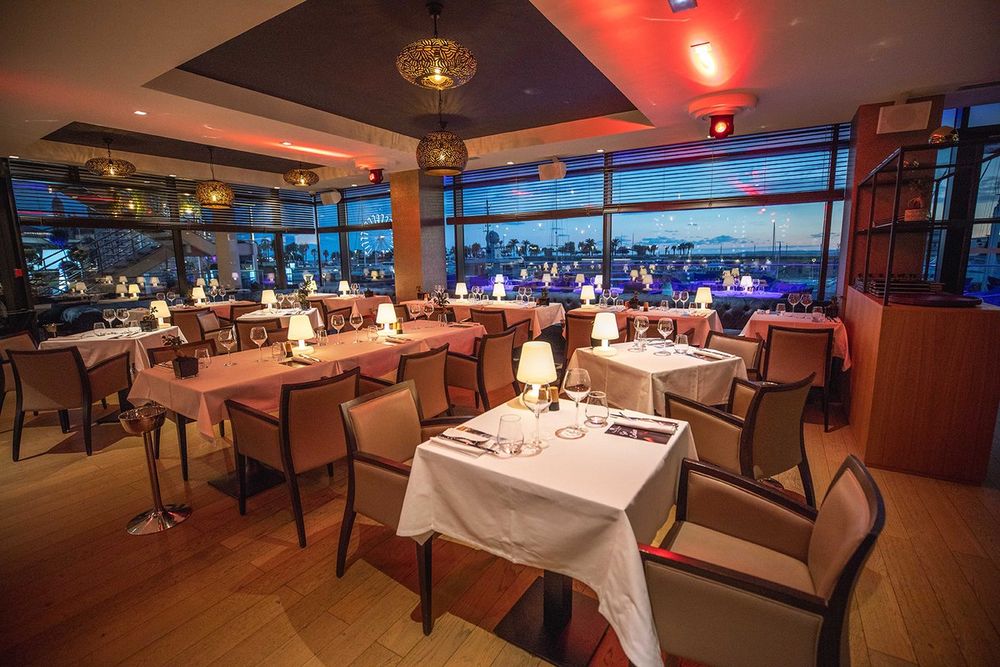 The dining room of Le Baïa at dusk, its picture windows looking over the lit-up harbour