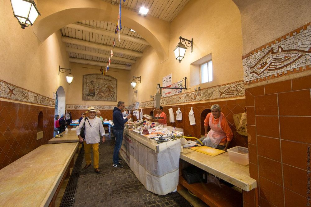 Shoppers at the fish stalls inside the tiled covered fish hall of Saint-Tropez