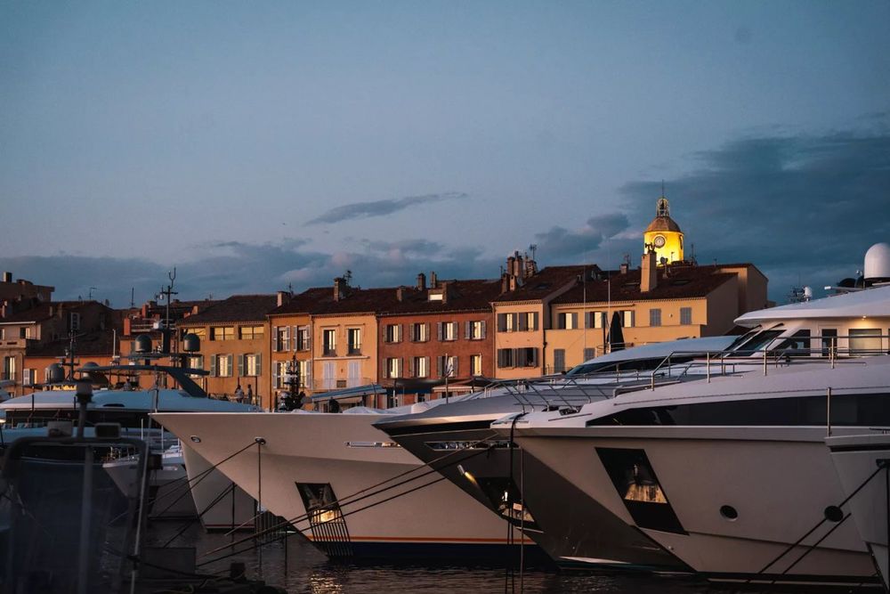 Yachts moored in front of the old port's houses and bell tower at dusk, seen from the Café de Paris