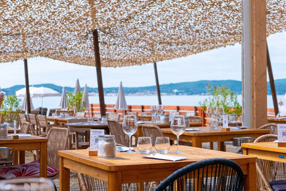Tables laid on the shaded terrace of Le Nino with the sea beyond