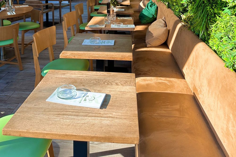 Wooden tables and banquettes under a living wall of flowers inside Nautik, Sainte-Maxime