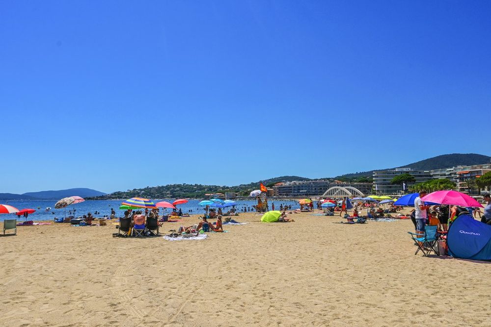 Parasols and sunbathers on the sand of the town-centre beach of Sainte-Maxime, the Maures hills behind