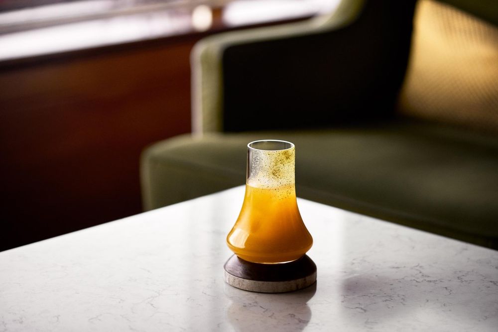 An amber cocktail on a marble table in front of green velvet armchairs at Cadierbaren, Grand Hôtel