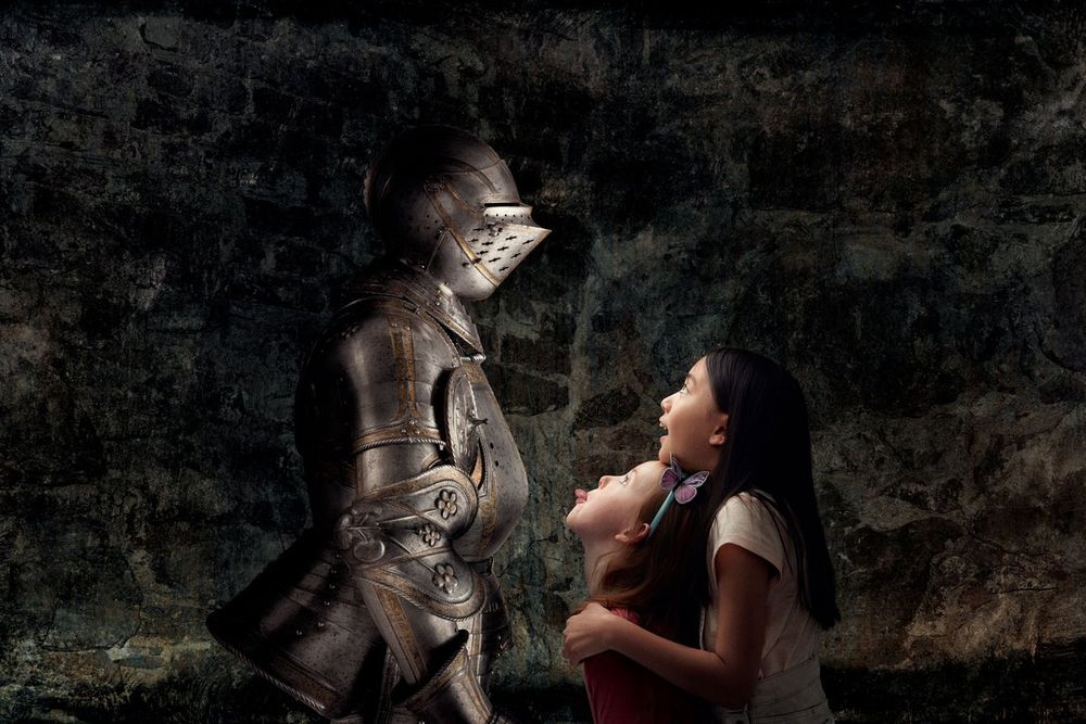 Two girls looking up in wonder at a figure in full armour against a stone wall at Livrustkammaren