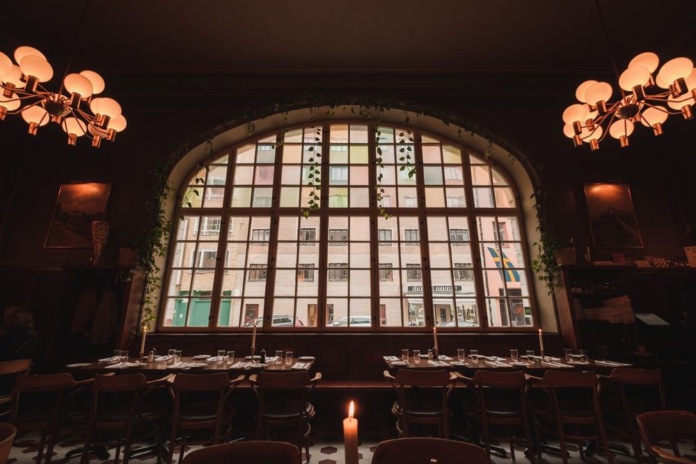 Candlelit tables under the great arched window and globe lamps in the main hall at Pelikan on Blekingegatan
