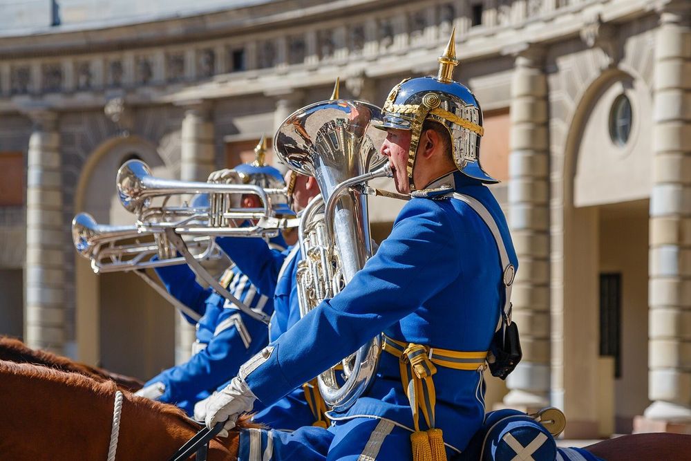 A mounted musician of the Royal Guard in a blue uniform and gilded helmet playing a brass instrument in the palace courtyard