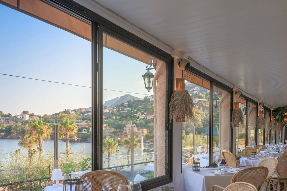 The glazed panoramic dining room of La Maréa, laid with white tablecloths, overlooking the sea and the Estérel