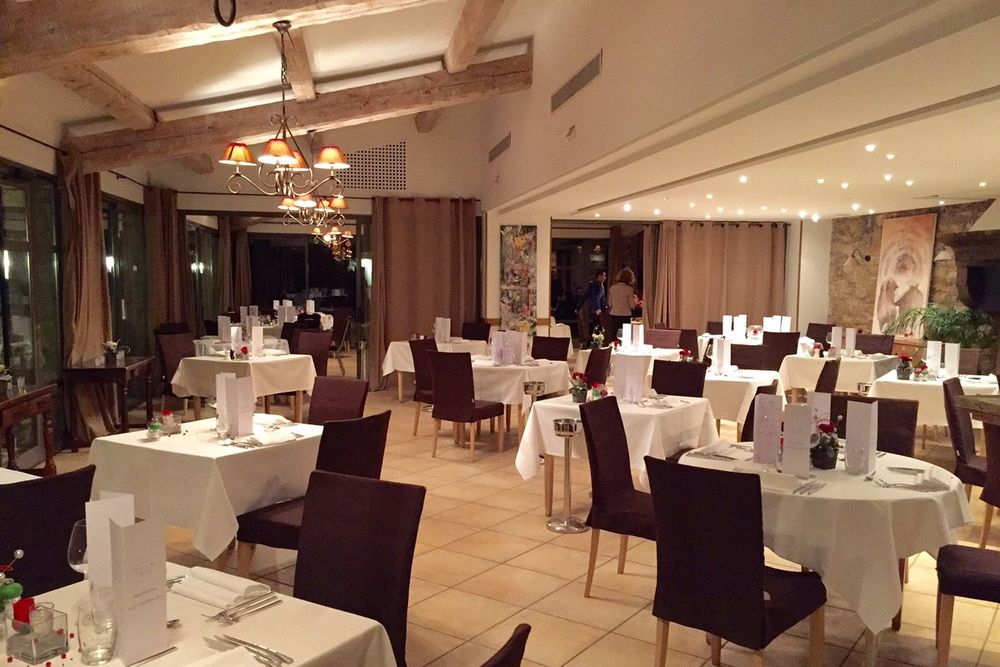 Laid tables under beams and chandeliers in the dining room of La Bégude restaurant