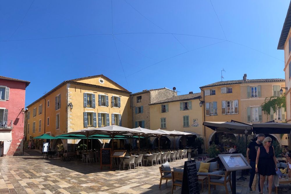 The Place des Arcades in Valbonne village with café terraces and pastel façades under a blue sky
