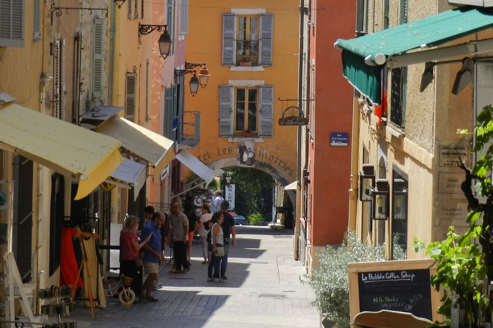 Shop awnings and strollers in a straight lane of Valbonne's grid village, with ochre façades