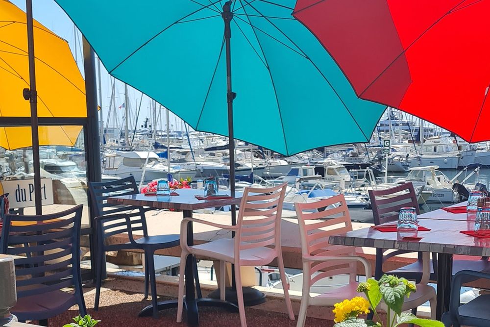 Colourful parasols and set tables on Le Jardin du Port's terrace above the boats of the Vieux Port, Golfe-Juan
