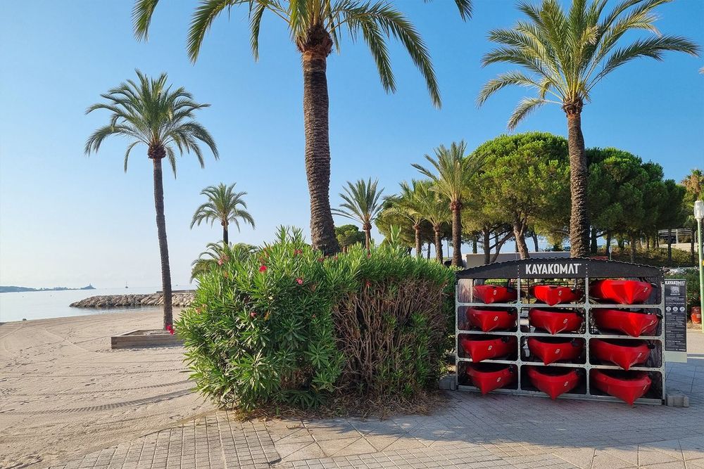 The Kayakomat self-service rack of red kayaks under palm trees on the Golfe-Juan seafront