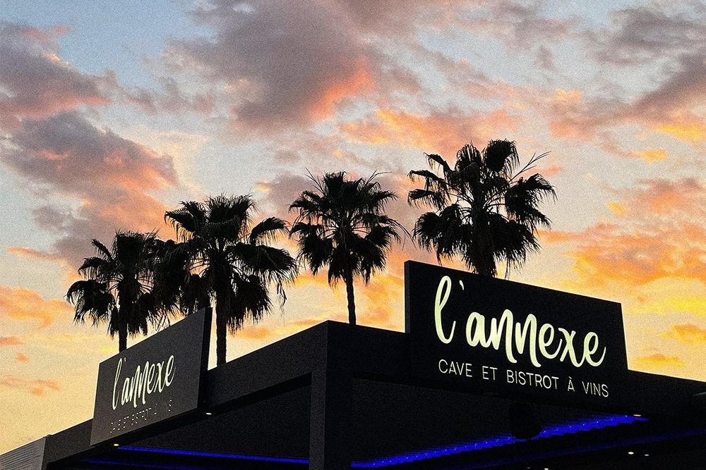 Palm silhouettes and a pink evening sky above L'Annexe, cave et bistrot à vins, at Port Camille Rayon