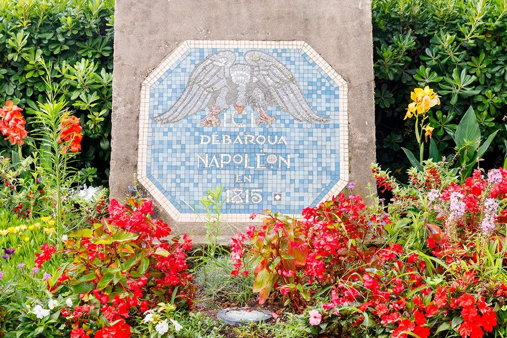 The Napoleon landing stele with its eagle plaque among red flowers on the Vieux Port of Golfe-Juan