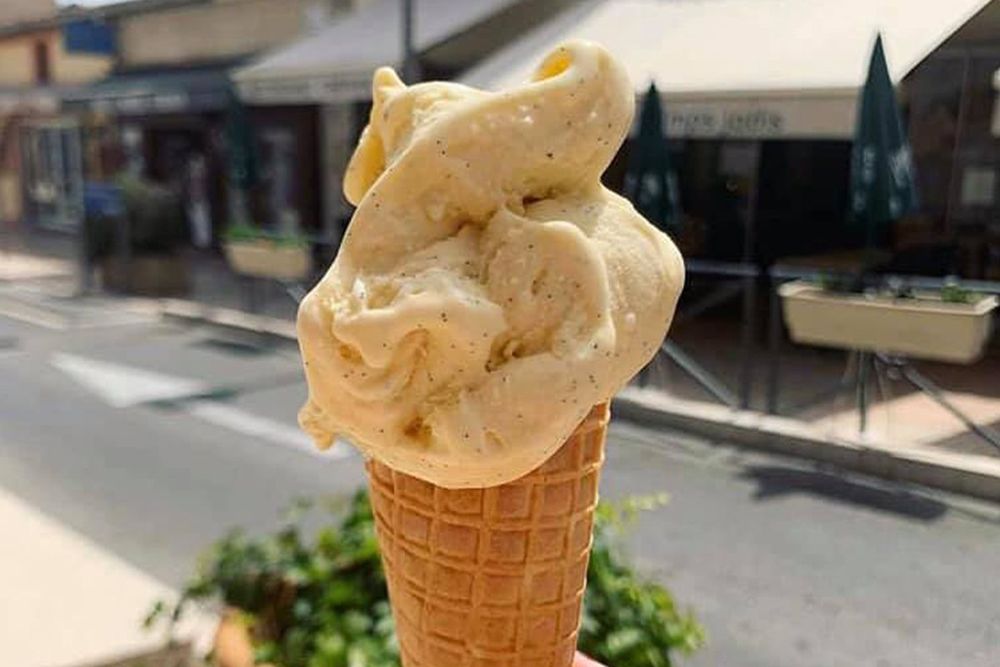 A cone of pale artisan ice cream held up in the street outside Le Temps Jadis in Vallauris
